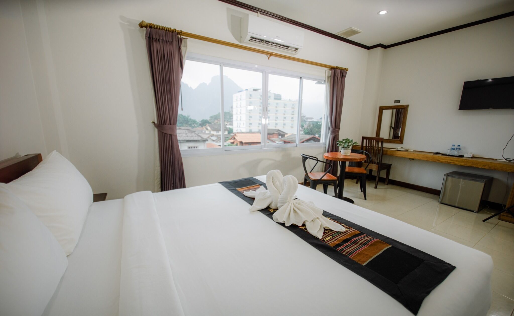 Habitación de hotel con cama, escritorio, silla, televisor y ventana con cortinas.