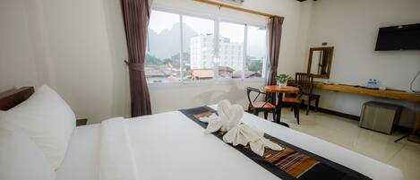 Habitación de hotel con cama, escritorio, silla, televisor y ventana con cortinas.