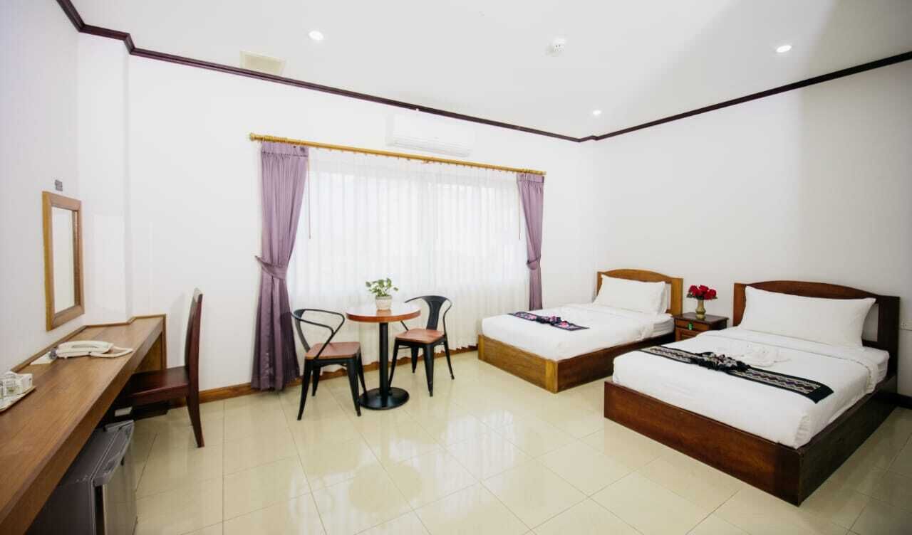 A hotel room with two beds, a desk with a telephone, a chair, a small table, and a window with curtains.