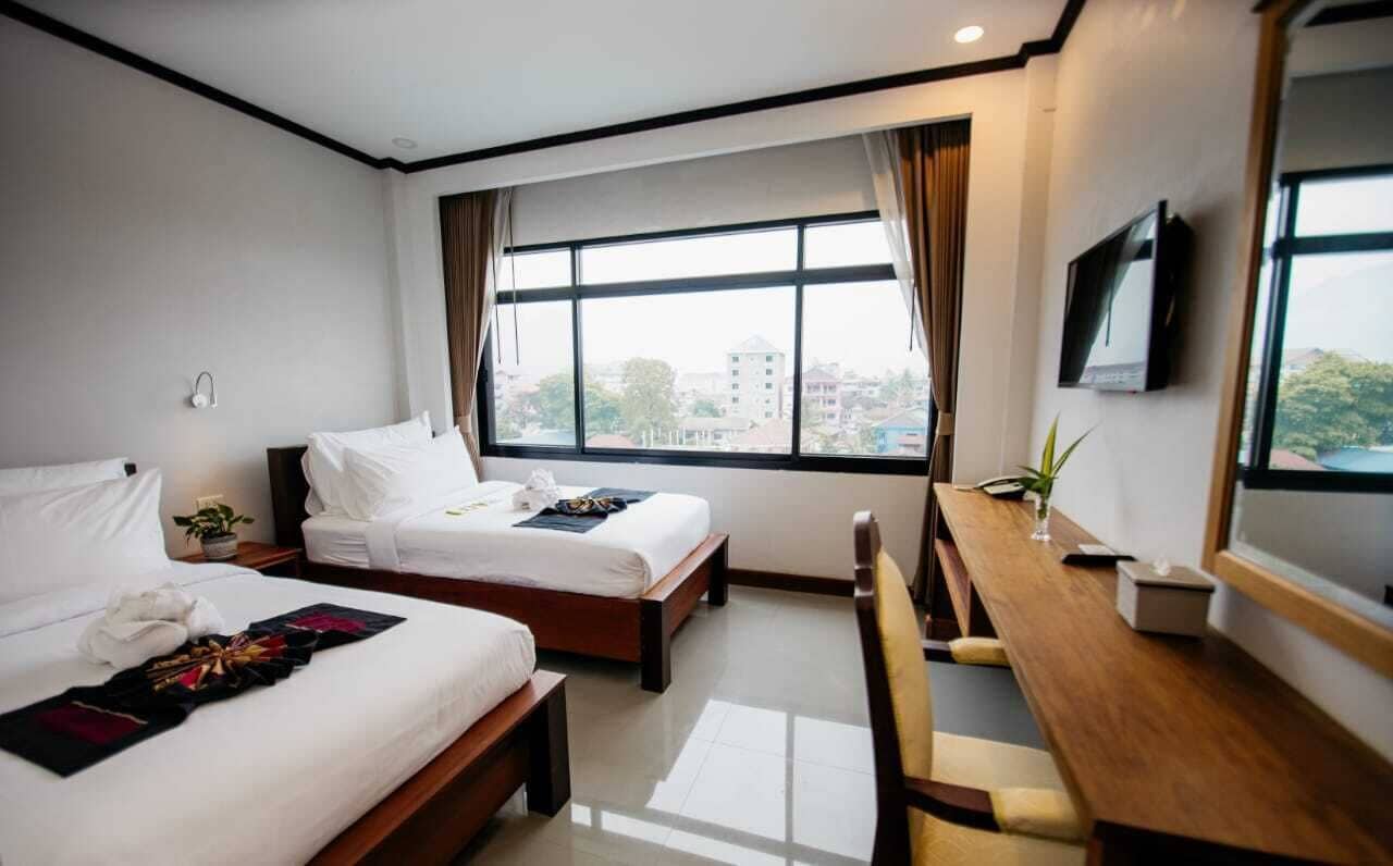 A hotel room with two beds, a desk, a TV, and a window with a city view.