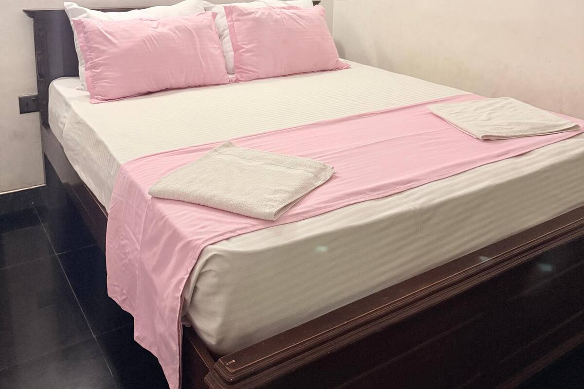 A neatly made bed with pink and white bedding, a wooden headboard, and two wall-mounted light fixtures.