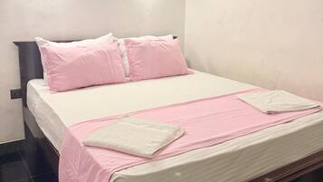 Una cama bien tendida con ropa de cama rosa y blanca, un cabecero de madera y dos lámparas fijadas a la pared.