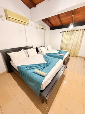 A room with two beds, each with white linens and teal bedspreads. There are ceiling fans and an air conditioning unit on the walls. - Venus Hotel (Colombo)