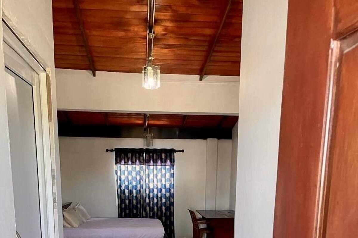 A bedroom with two beds, a wooden ceiling, a tiled floor, and a red doormat.