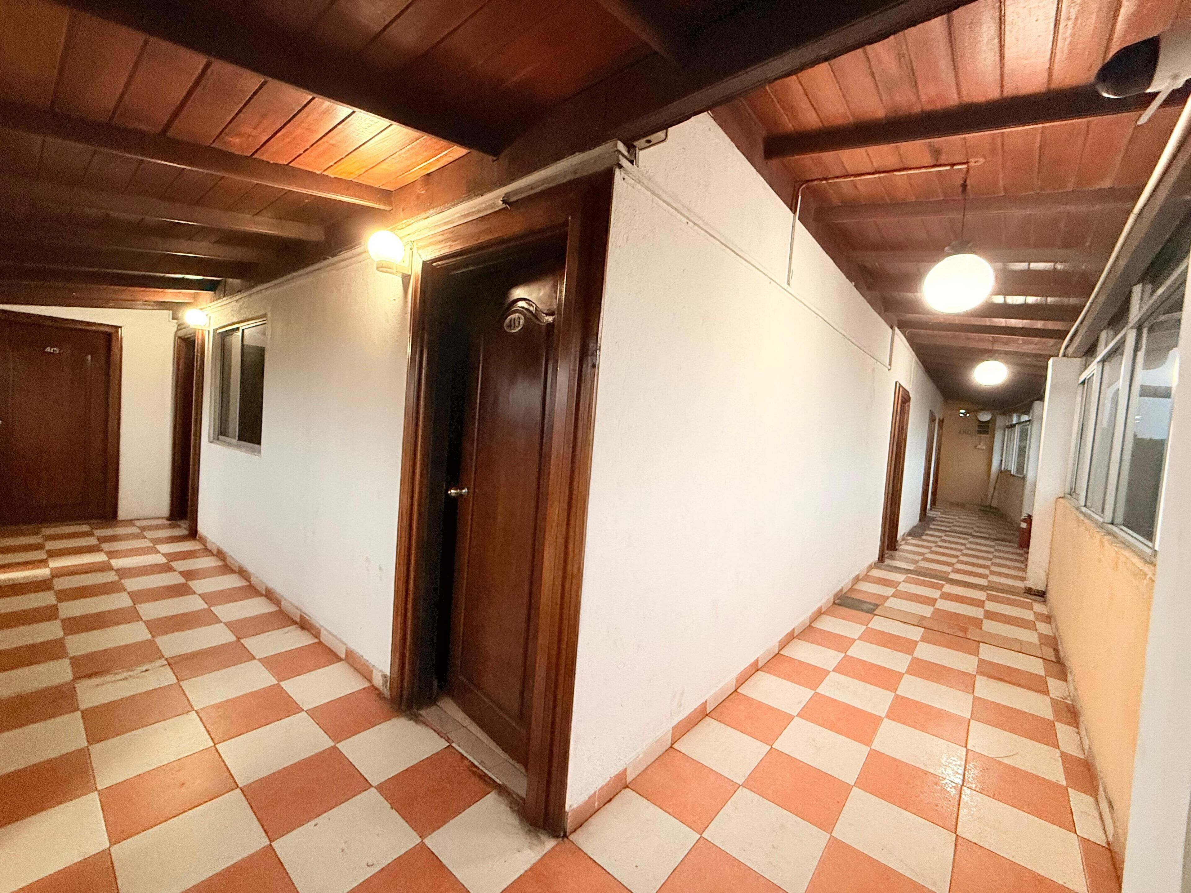 A corridor with checkered flooring, wooden doors, and a ceiling with exposed beams.