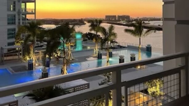 A balcony with a view of a swimming pool and palm trees, overlooking a sunset over a body of water. - View with a View Waterfront WiFi,Furnished,Beaches,New Modern (Tampa)