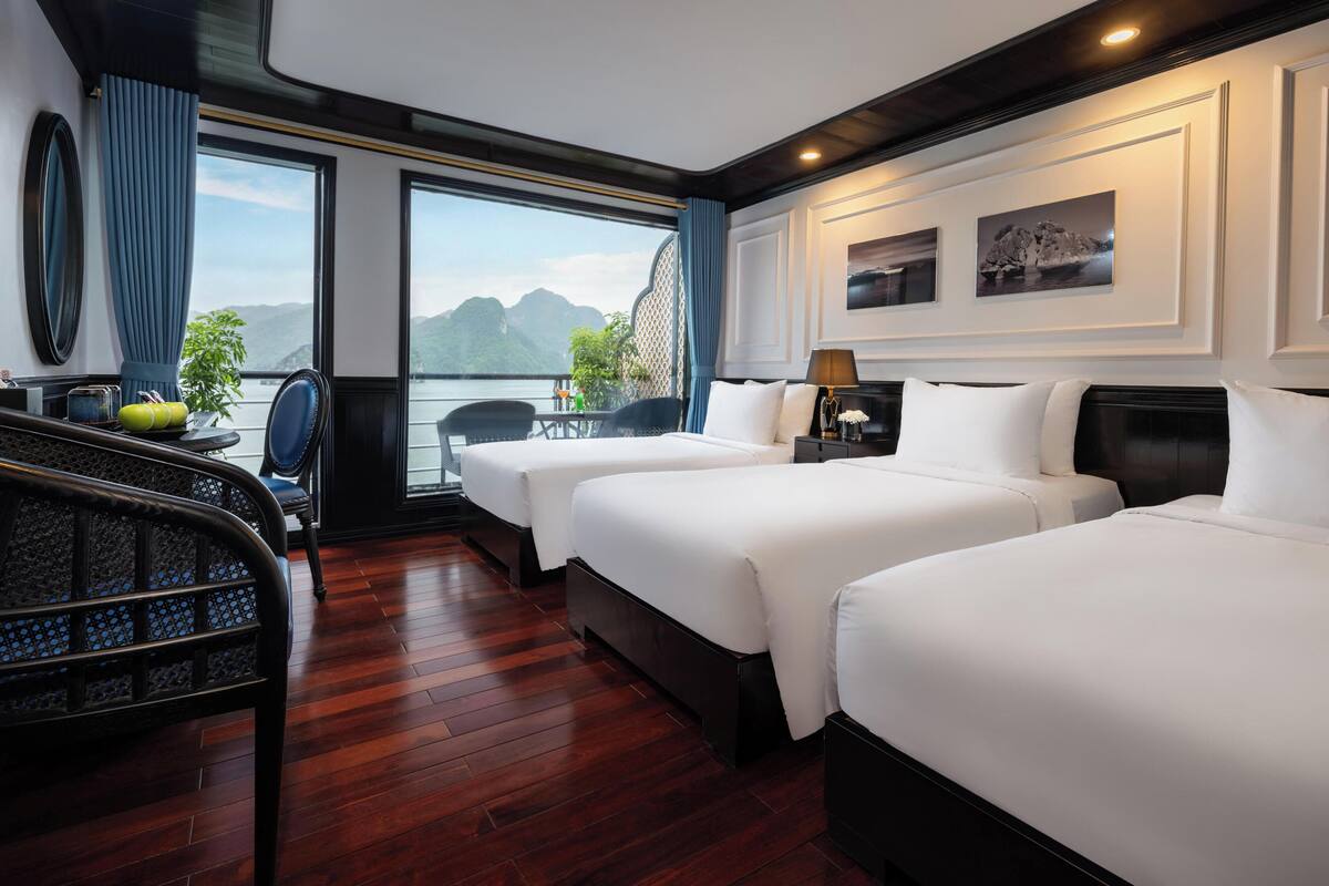 Une chambre d’hôtel avec deux lits, un coin salon comprenant un fauteuil et une table, et une vue sur les montagnes.