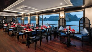 A restaurant with tables set for dining, large windows with a view of the water, and a ceiling with recessed lighting. - La Casta Cruise (Tuan Chau)