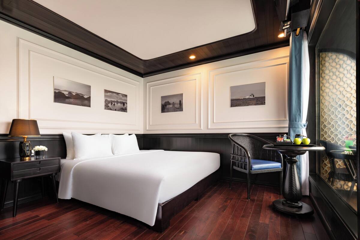 Une chambre d’hôtel avec un grand lit, une table de chevet, une chaise et une table sur laquelle se trouve un plateau de fruits.