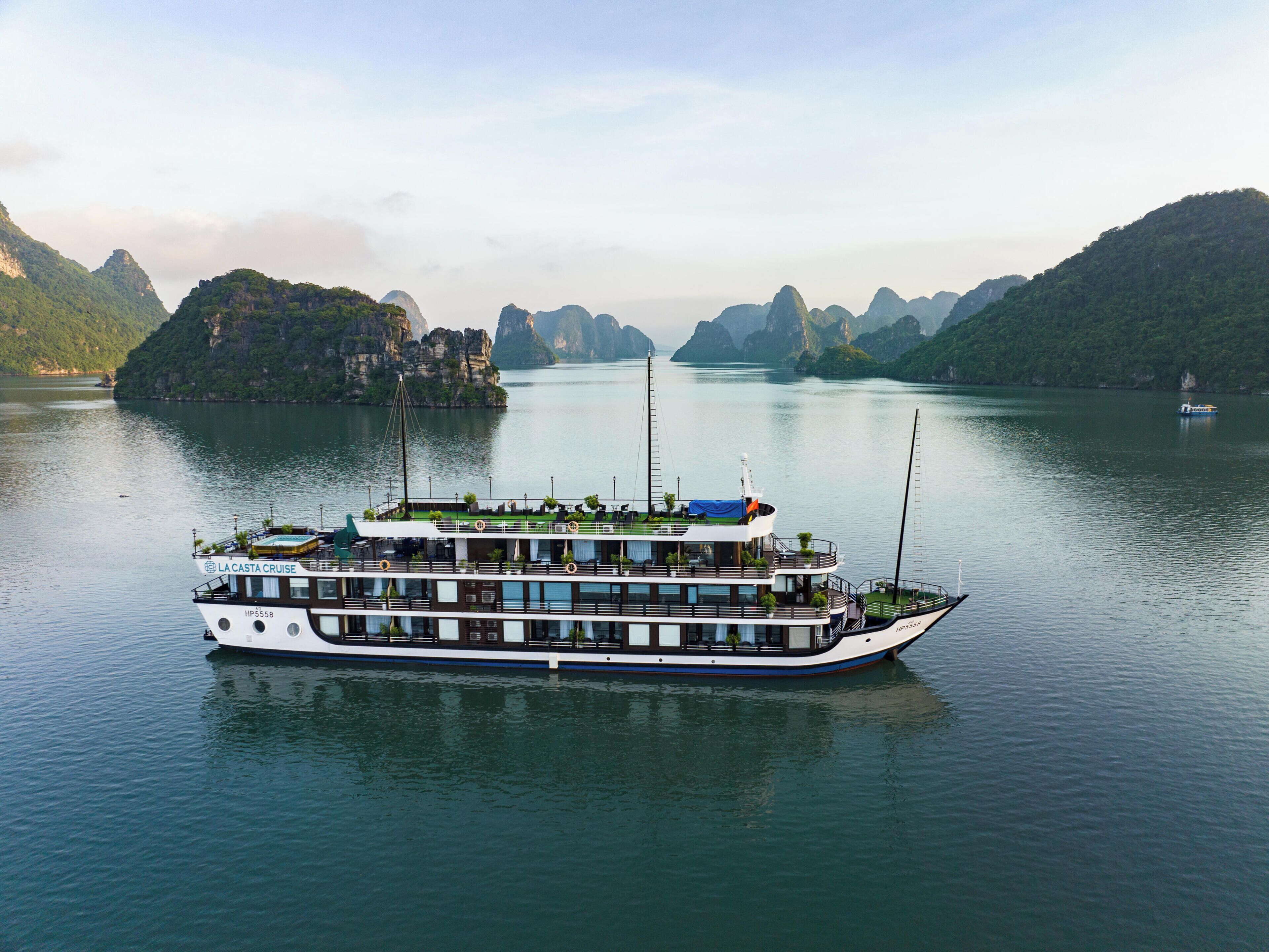 A large cruise ship with multiple decks and a swimming pool, surrounded by calm water and mountainous landscape.