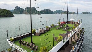 A deck with outdoor seating, a lifeboat, and a view of the water and mountains. - La Casta Cruise (Tuan Chau)