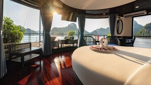 A room with a large bed, a table with a swan-shaped centerpiece, a view of the water, and a balcony with chairs. - La Casta Cruise (Tuan Chau)