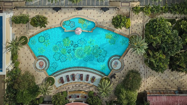 Vista aerea di un resort con piscina, palme e spiaggia.