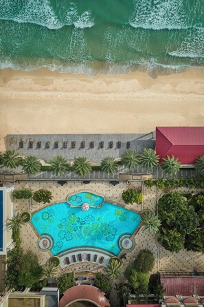 An aerial view of a resort with a pool, palm trees, and a beach.