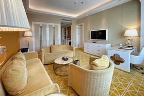 A hotel room with a sofa, armchair, TV, bedside table, and a patterned floor. - Ramada by Wyndham Sihanoukville Xinhaohui Palace (Sihanoukville)