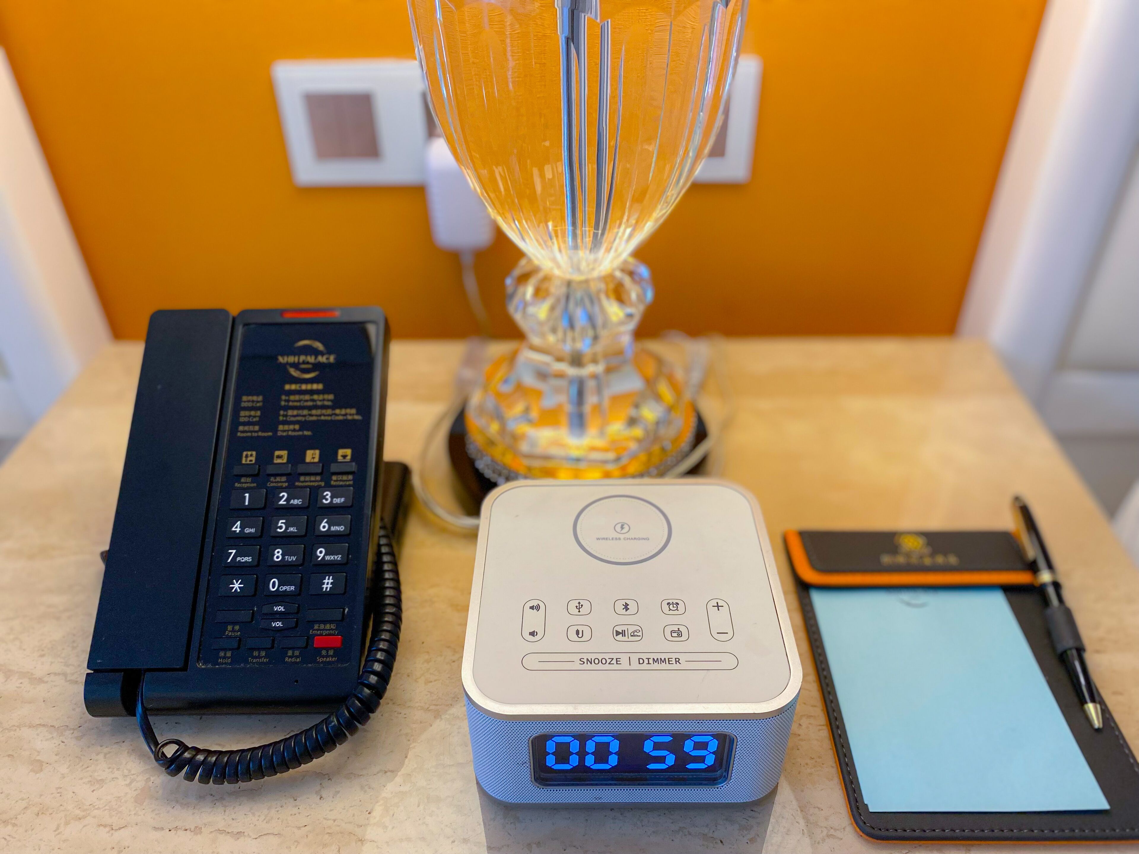 A hotel room with a telephone, a digital clock, a lamp, and a notepad on the counter.