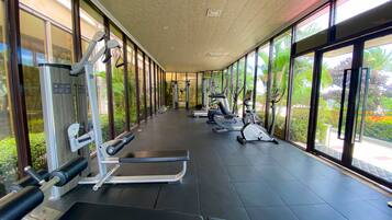 A gym with various exercise equipment, large windows, and a view of greenery outside.