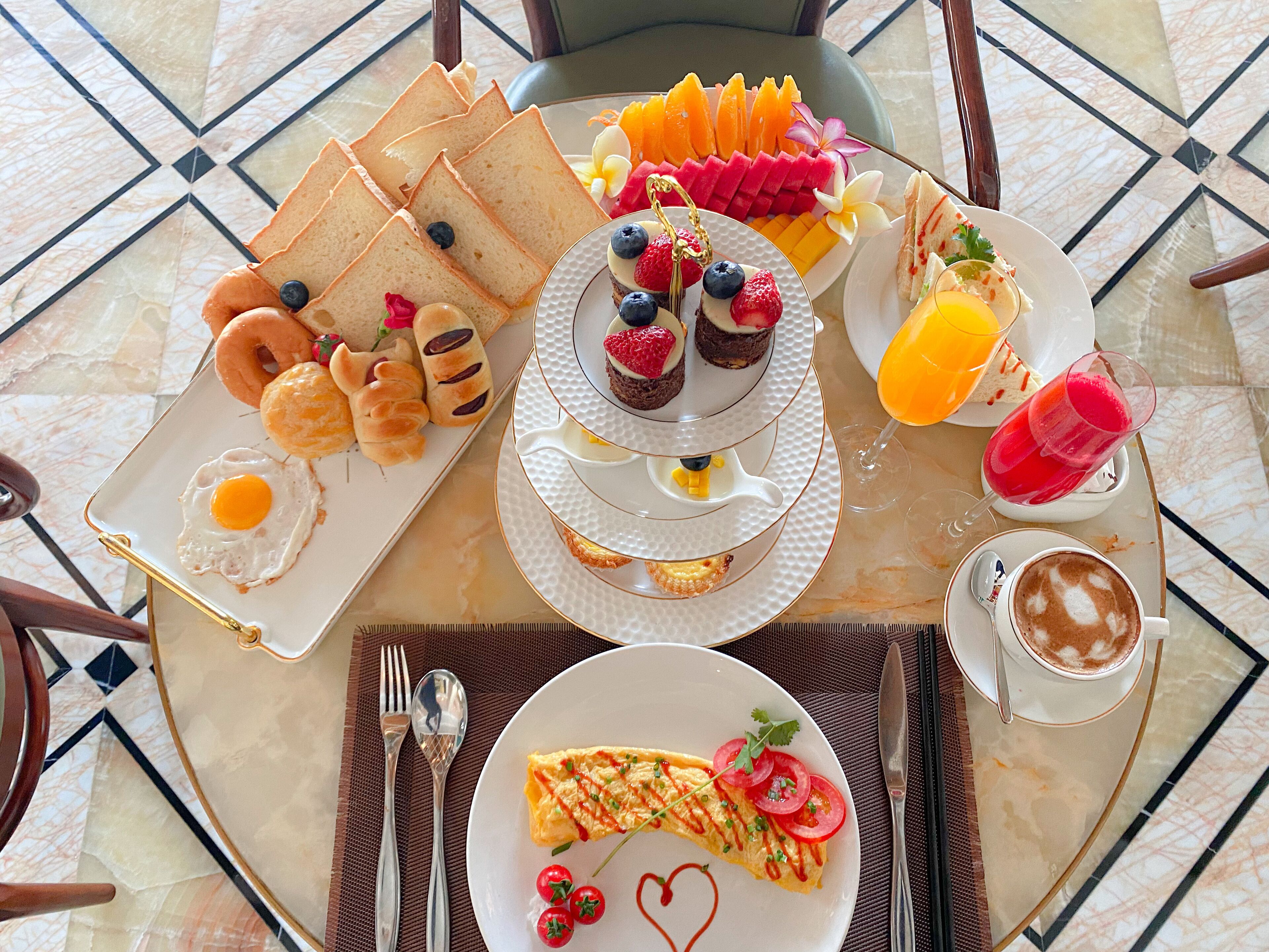 A breakfast buffet with various dishes including eggs, pastries, fruit, and beverages.