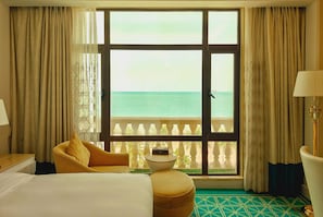 A hotel room with a bed, a yellow armchair, a small round table, and a view of the sea through large windows. - Ramada by Wyndham Sihanoukville Xinhaohui Palace (Sihanoukville)
