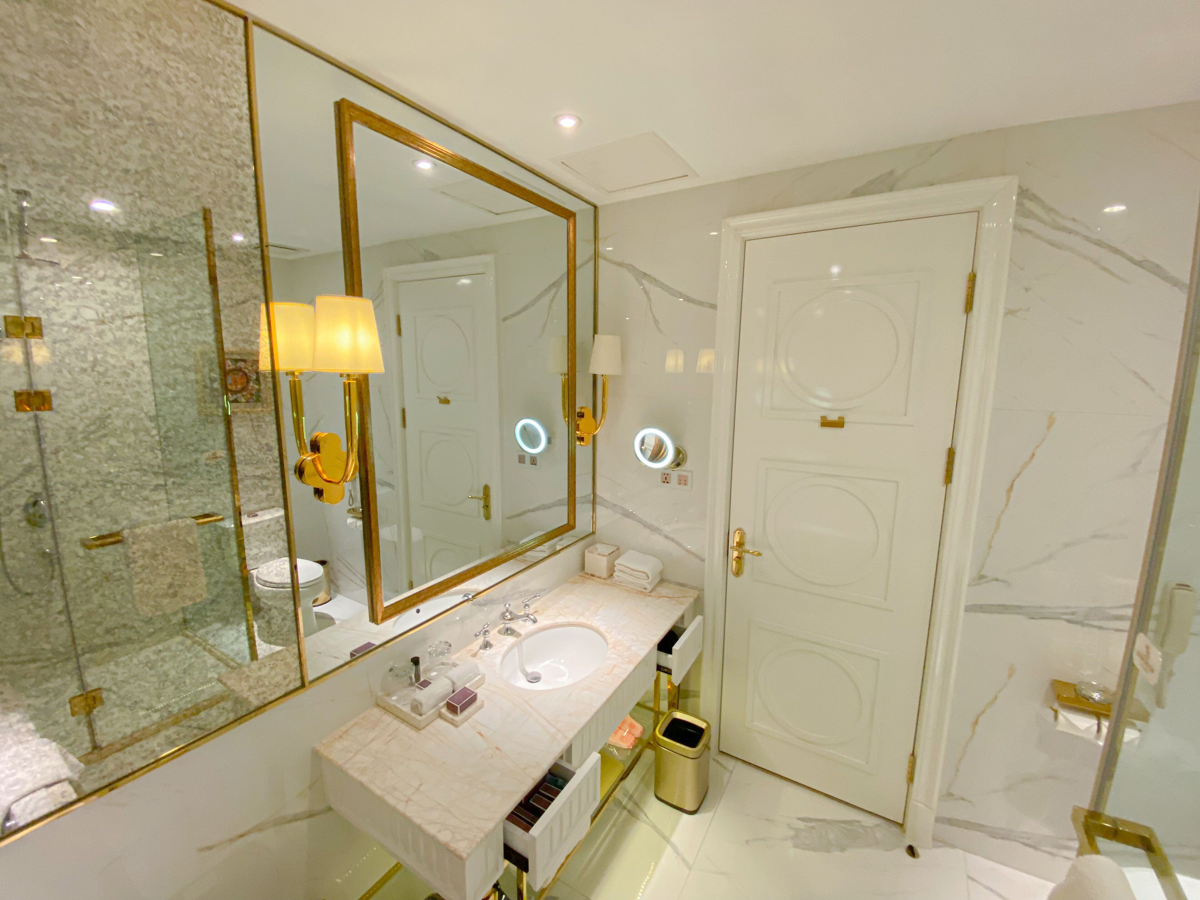 A bathroom with a large mirror, a sink, a toilet, and a door.