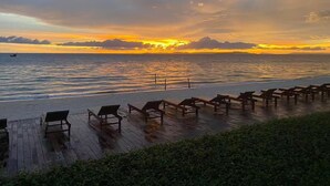 Una terrazza in legno con panchine che si affaccia su una spiaggia al tramonto.