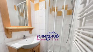 Une salle de bain avec un lavabo blanc, des meubles en bois, un miroir et un espace douche doté d’une porte en verre.