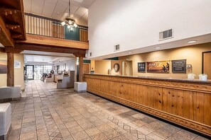 Uma área de recepção com balcão de madeira, piso de azulejos e vista para o lobby.