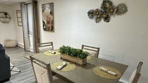 A dining area with a rectangular table, four chairs, and a decorative plant centerpiece. - Hamptons Apartment (East Quogue)