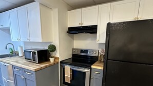 A modern kitchen with white cabinets, a black refrigerator, a microwave, and an oven. - Hamptons Apartment (East Quogue)