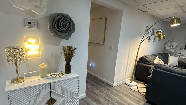 A modern living room with a grey sofa, a white console table with geometric patterns, a large grey rose decoration, and a floor lamp. - Hamptons Apartment (East Quogue)