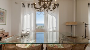 A dining area with a glass table, wicker chairs, a chandelier, and a view of the sea. - Spectacular apartment in Mont-roig (Mont-roig del Camp)