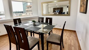 A dining area with a glass-top table, dark wooden chairs, and a view of a cityscape through large windows. - Apartamento en San Isidro - A un paso del Golf! (San Isidro)