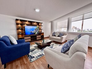 A modern living room with a flat-screen TV, wooden shelving, and a sofa set.