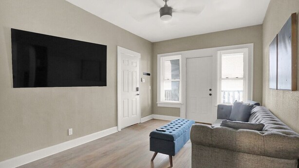 Una sala de estar con un sofá gris, un reposapiés azul y un televisor de pantalla plana montado en la pared.