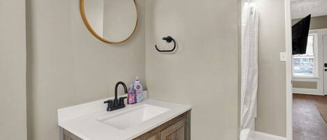 A bathroom with a white sink, wooden cabinets, a round mirror, and a black towel rack.