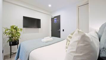 Habitación de hotel con cama, televisor de pantalla plana montado en la pared, puerta con un letrero y una planta en maceta.