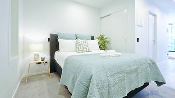 Un dormitorio con cama, mesita de noche, lámpara y planta en maceta.