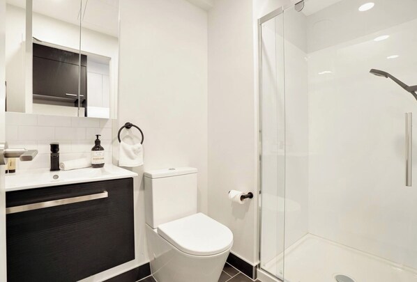 A modern bathroom with a glass shower enclosure, a toilet, a sink with a mirror, and a dark-colored cabinet.
