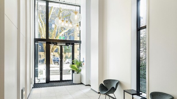 Ett modernt receptionsområde med en entré som har en glasdörr, en krukväxt och två svarta stolar.