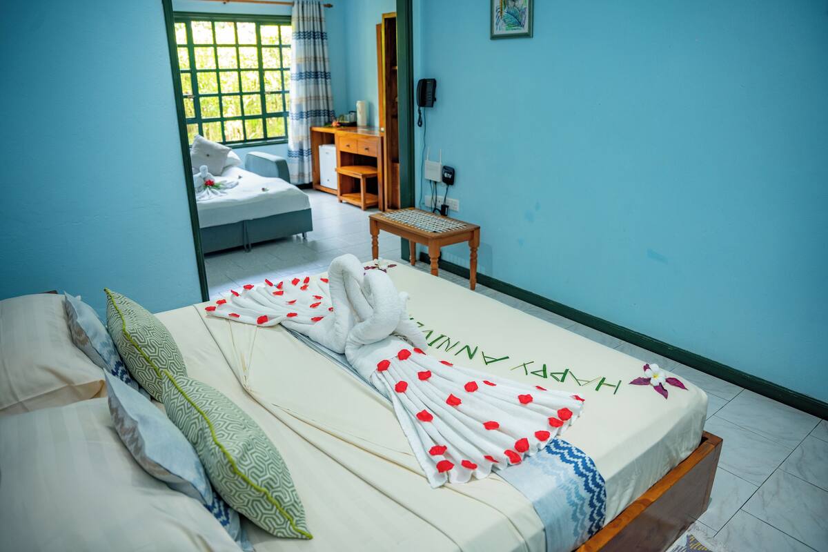Habitación de hotel con cama, escritorio, silla y baño visible a través de una puerta abierta.