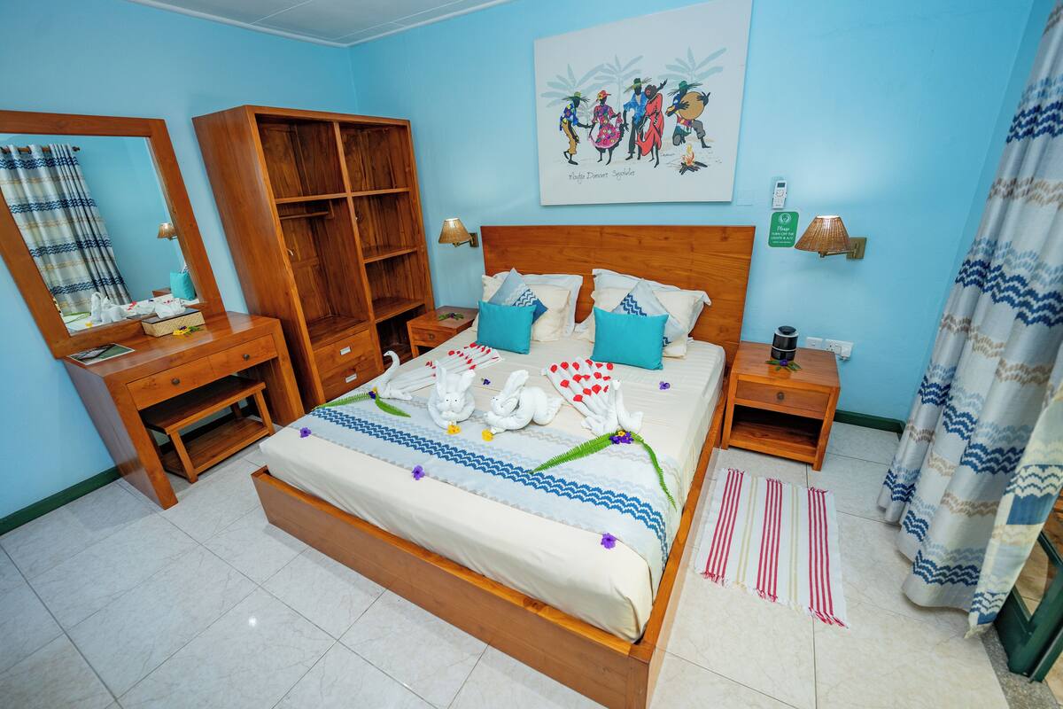 Un dormitorio ordenado con una cama de madera, una mesita de noche, un aparador, un espejo y un estante en la pared.