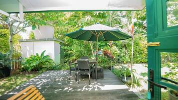 An outdoor patio with a wooden table and chairs, a green umbrella, and potted plants.