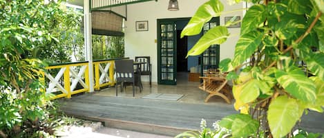 A covered outdoor area with wooden flooring, a yellow and white fence, and various plants.