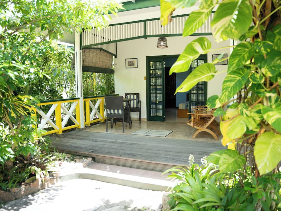 A covered outdoor area with wooden flooring, a yellow and white fence, and various plants.
