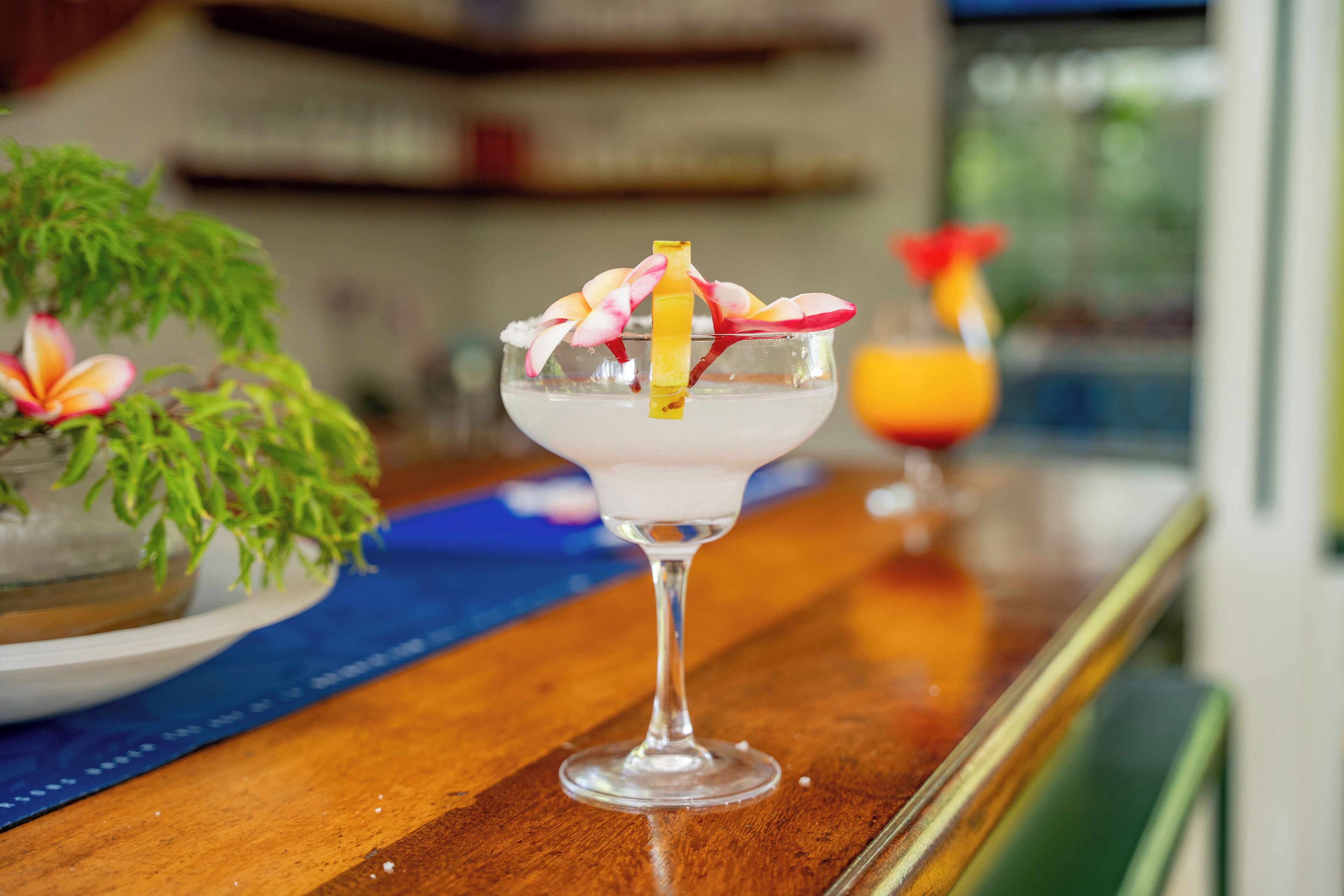 Un verre à cocktail, agrémenté d’une décoration de fruits, posé sur le comptoir en bois d’un bar.