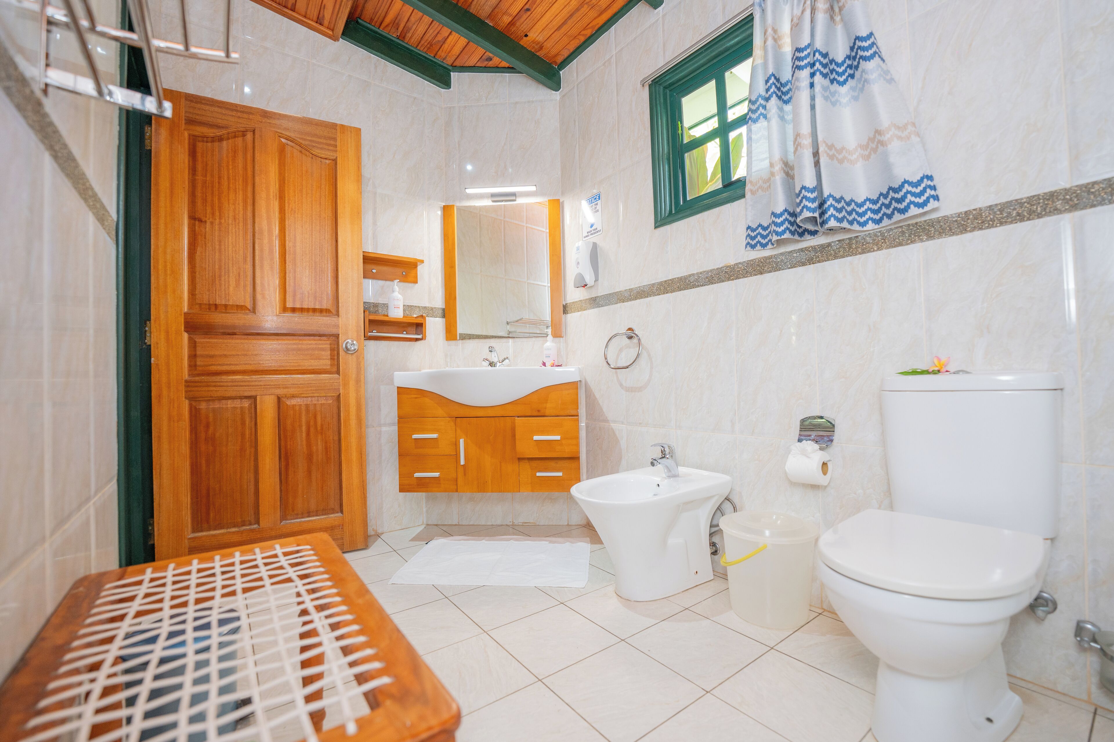 Casa de banho com porta de madeira, pia, bidé, sanita e espelho.
