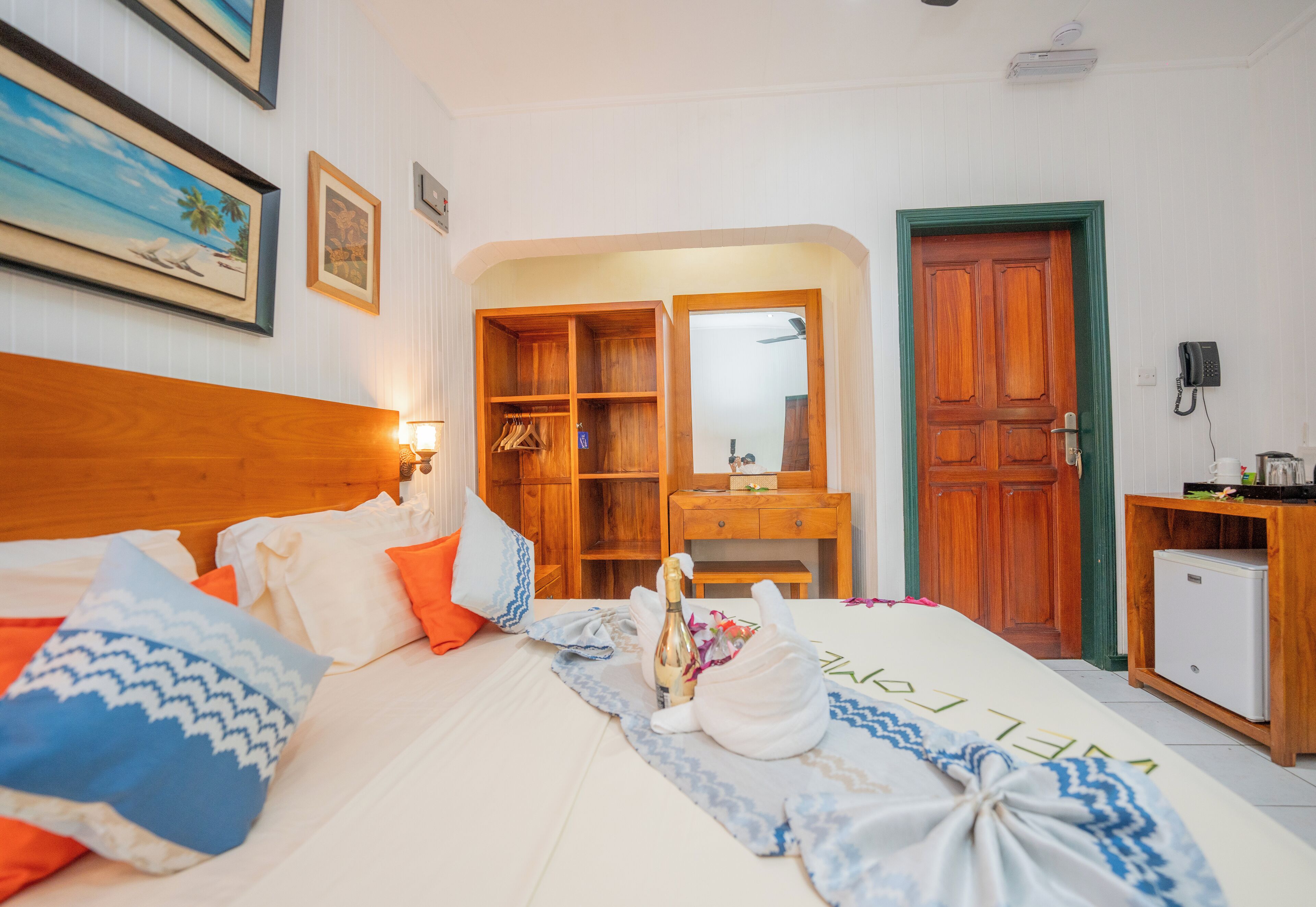 Habitación de hotel con cama, armario de madera, pequeño escritorio con refrigerador y baño visible a través de una puerta abierta.