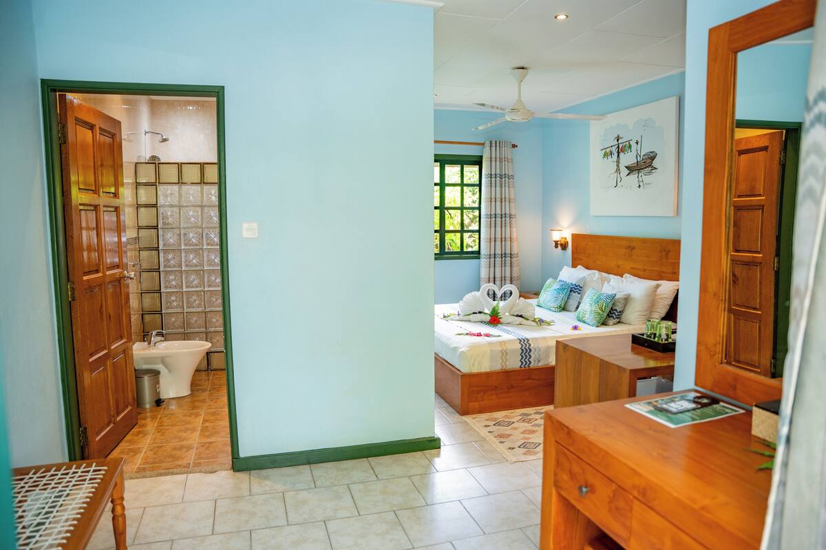 Un dormitorio con cama, mesita de noche, espejo, ventana y baño con inodoro y lavabo.