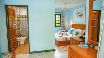 A bedroom with a bed, a bedside table, a mirror, a window, and a bathroom with a toilet and sink.
