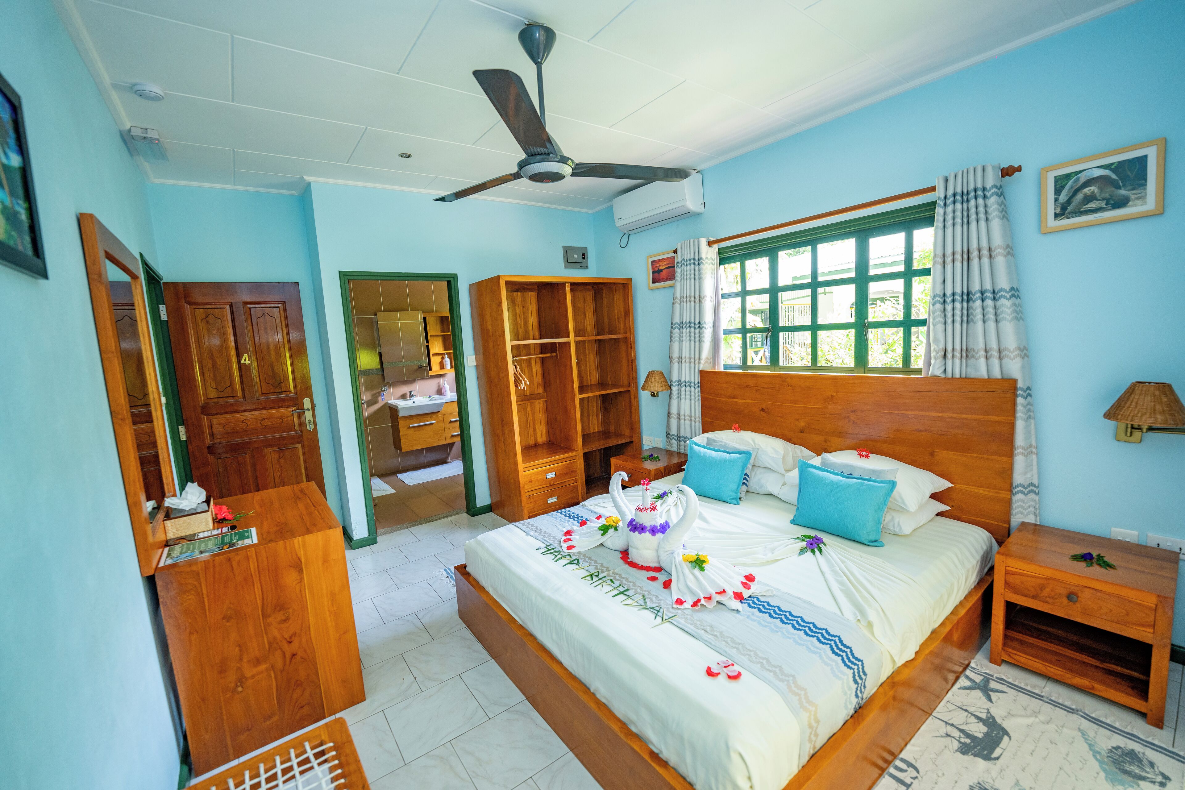 A bedroom with a wooden bed, a ceiling fan, a window with curtains, and a bedside table.